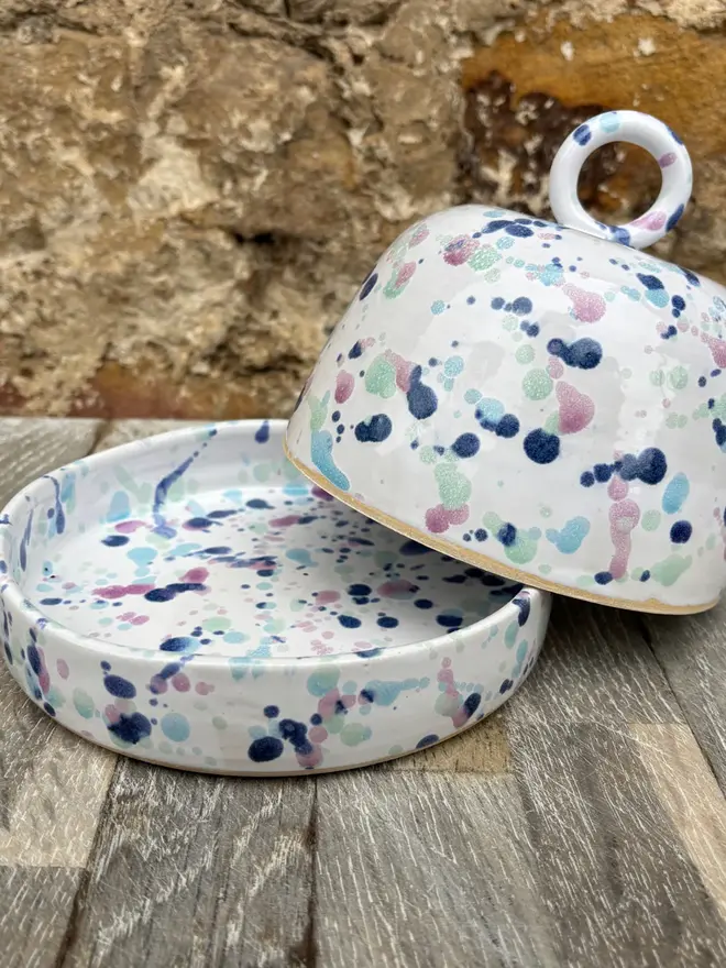 Sweetpea Butter Dish, a colourful butter dish sitting on a wooden surface against a brick backdrop. 