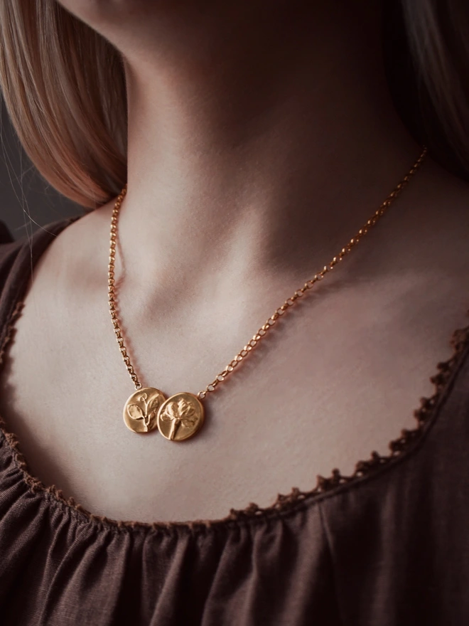 24ct Gold plated sterling silver double coin with primrose and sweet pea flowers worn by a model