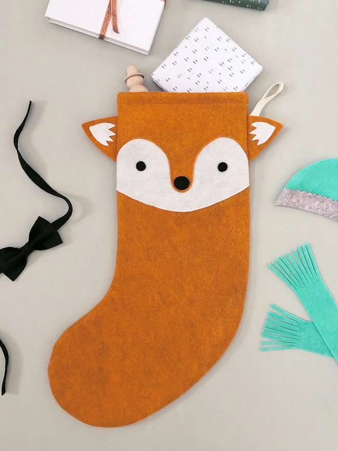 A handmade felt fox stocking lays on a grey surface with several gifts poking out from the top.