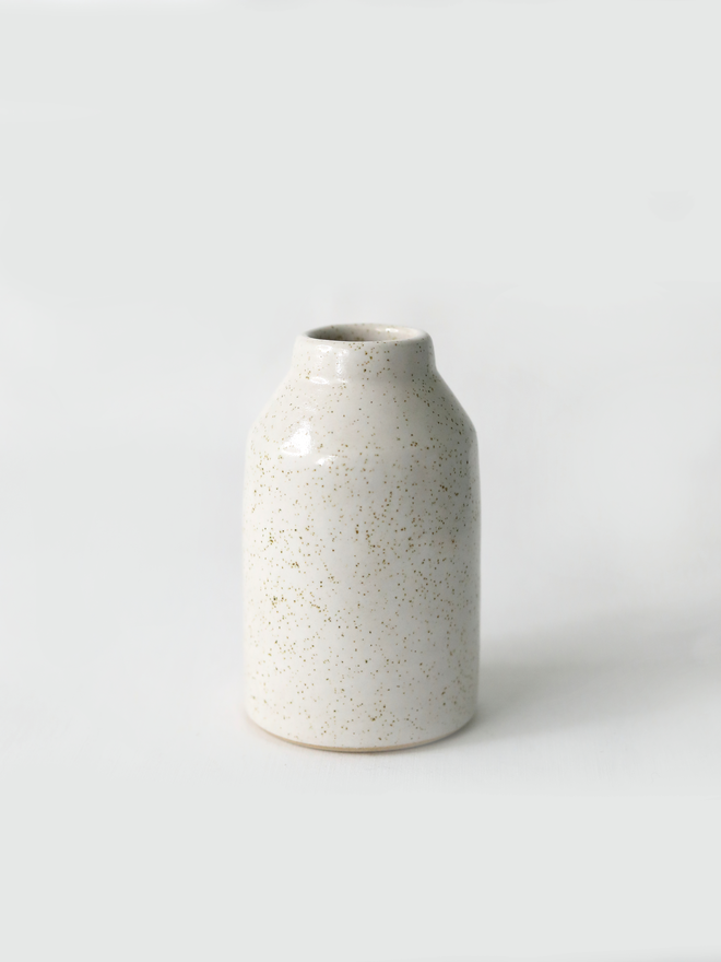 A small handmade ceramic bud vase in glossy pepper white glaze, with a rounded bottle shape and narrow neck, photographed against a plain white background