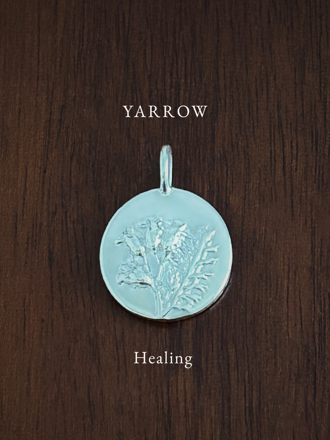 Sterling Silver Yarrow Coin Charm on a dark background with the language of flowers meaning, healing