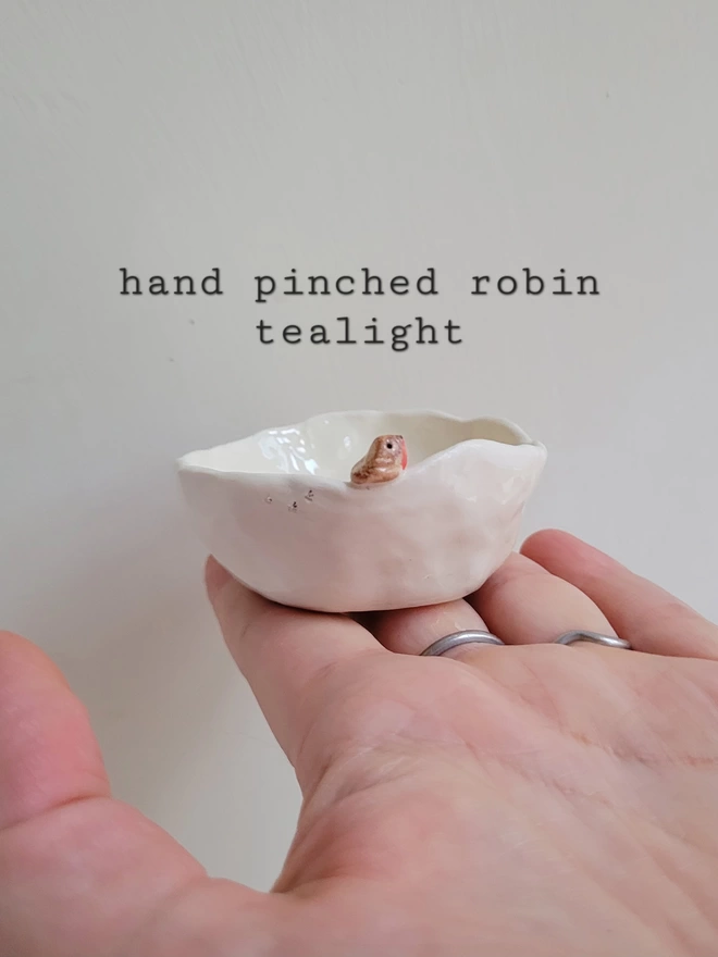 hand pinched off white pottery trinket pot with a tiny robin bird sculpture perched on the rim and tiny bird prints etched into the ceramic held in a hand