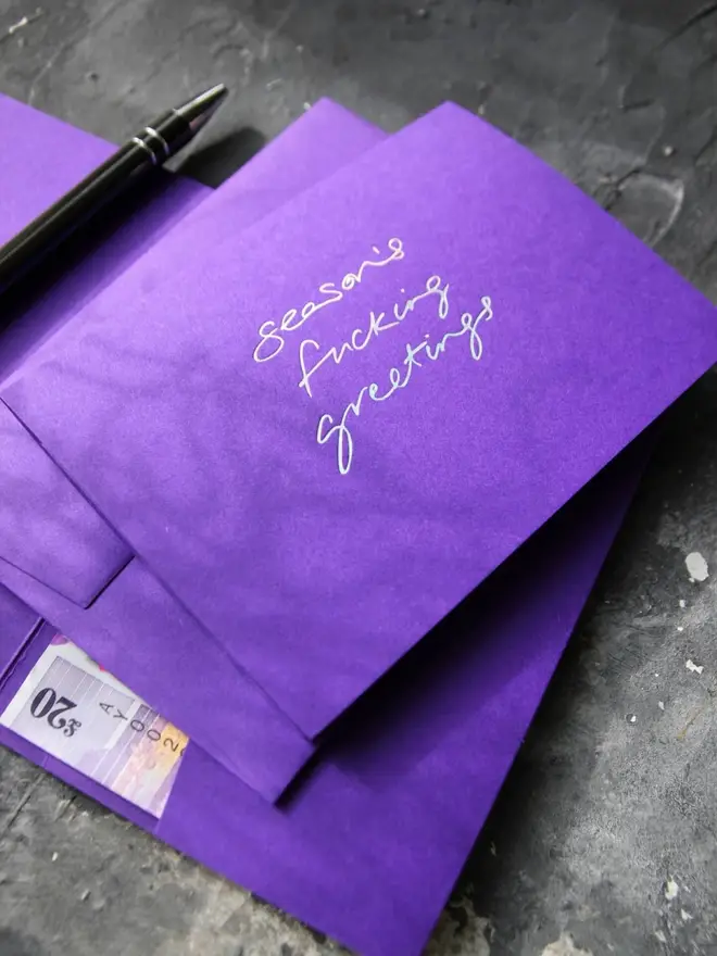 Hand foiled cash card or money wallet in a royal purple colour handfoiled in shiny holographic text which says 'season's fucking greetings'.