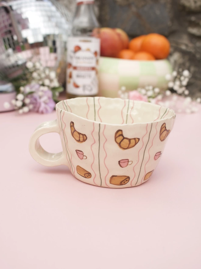 handmade stoneware mug decorated with handpainted croissants, coffee cups and pain au chocolat in a striped pattern