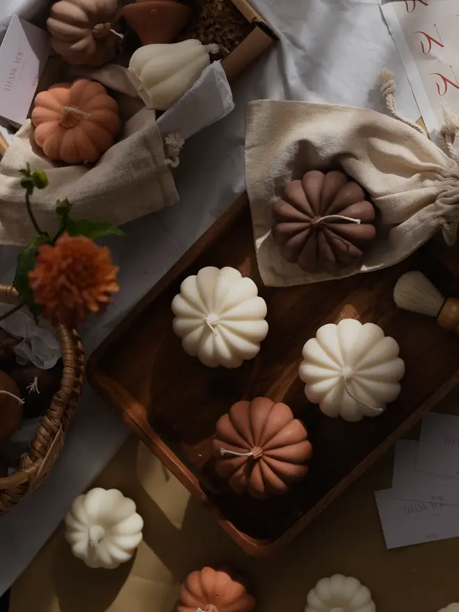 Extra Large Classic Dark Brown Wax Pumpkin Candle. A flat lay of cream, terracotta and brown pumpkin candles on a wooden tray, with linen gift bags, a gift box, dahlias and thank-you cards. The coordinating sculptural candles make thoughtful autumn gifts and a cosy display for harvest gatherings.