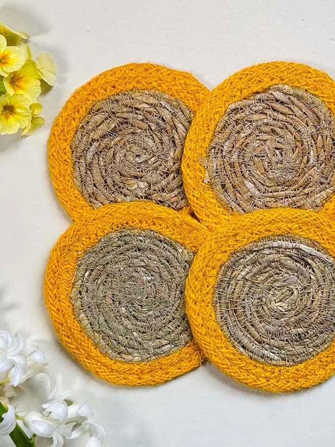 Seagrass coaster with yellow rings, shown on a light surface with yellow  flowers. 