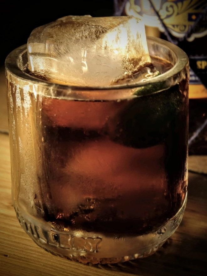 Whitby Dark Spiced Rum - RNLI Edition, a glass of rum sitting on a wooden surface indoors. 