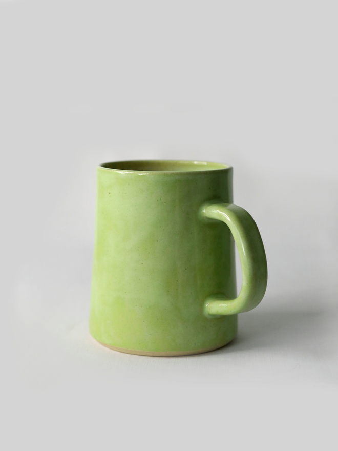 A handmade ceramic pint mug in spring green glaze with a chunky loop handle, photographed against a plain light grey background