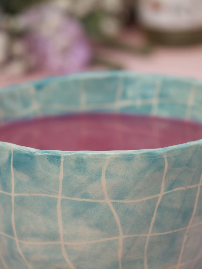 Swimming pool design on a stoneware handmade pottery mug in a bright turquoise blue grid pattern with bright pink liquid inside