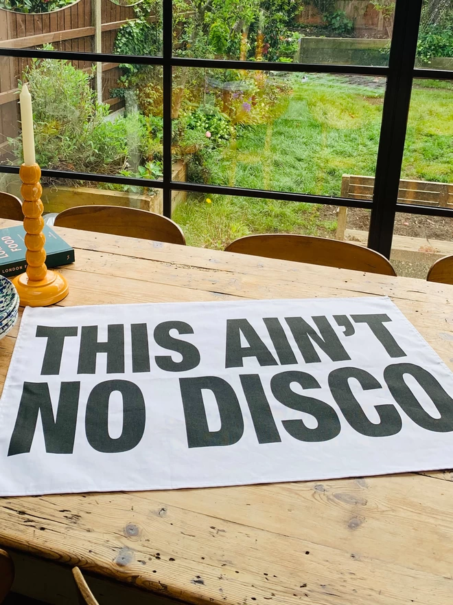 London Drying This Ain't No Disco black screen printed text on white tea towel laying on wooden kitchen table