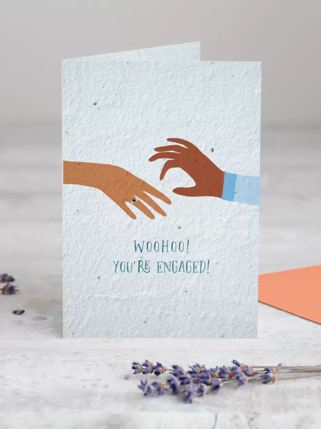 Seeded Paper Greeting Card featuring an illustration of a hand placing a ring on another hand with ‘WooHoo You’re Engaged’ underneath with a sprig of Lavender placed in the foreground of the image
