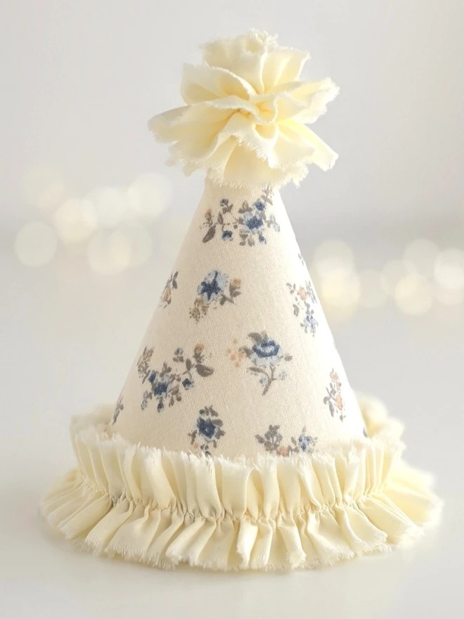 Handmade vanilla floral party hat with blue ditsy floral print and soft cotton pom-pom from the Mabel Collection.
