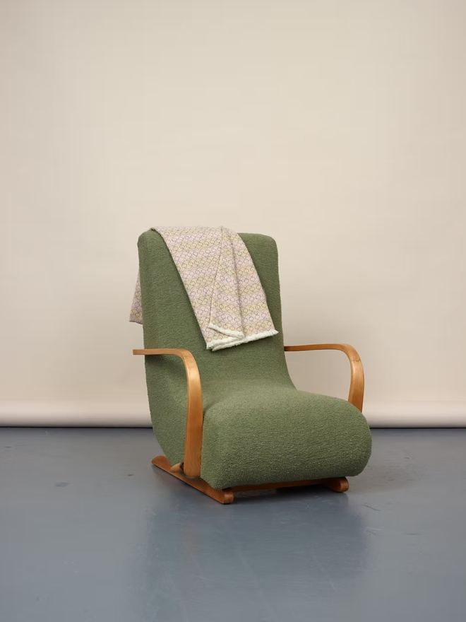 cairmeal lambswool blanket. a pink and brown blanket thrown over a green chair.