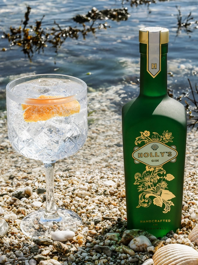 A large gin and tonic next to Holly's Gin bottle on the beach