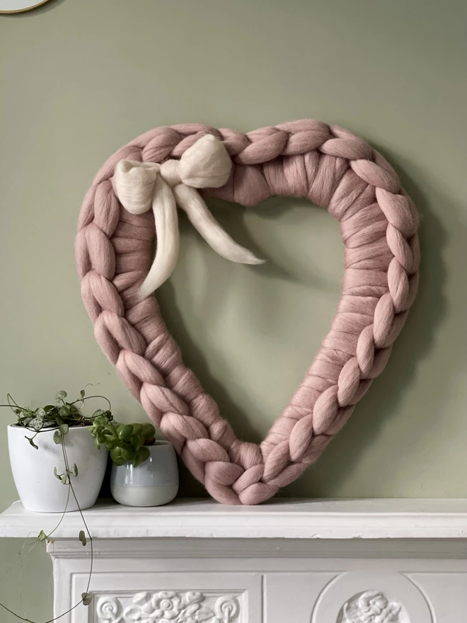 A mink pink woolly heart wreath sitting on a white mantel