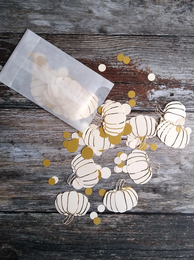 Pack of cream pumpkin table confetti spilling out of glassine packet onto wooden table