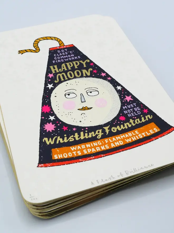 A Flash Of Brilliance Moon Firework Screenprint, a colourful firework design in the centre of a white screenprint. It is piled on top of more screenprints. 