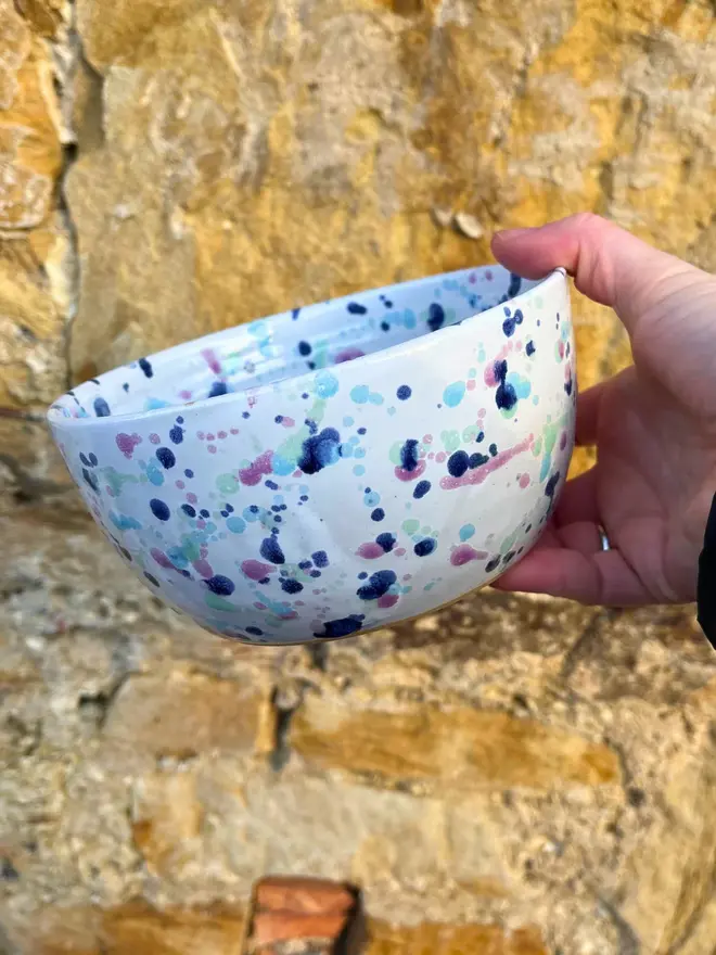 Sweetpea Small Bowl, a person holding a colourful bowl against a brick wall. 