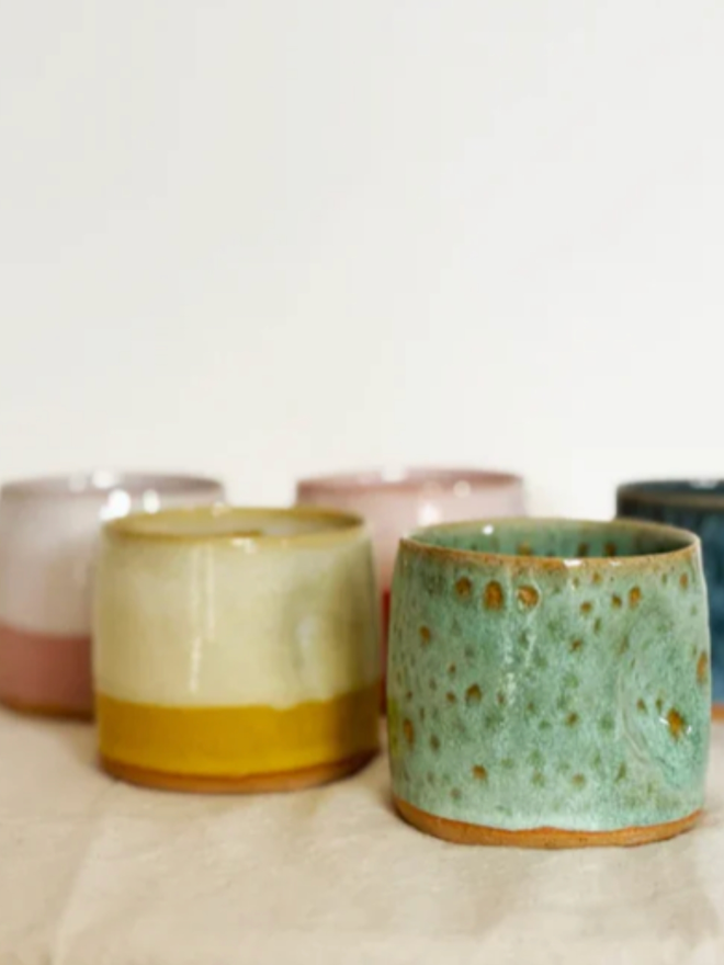 Pinch Mug. A view of five Mini Pinch Mugs in Green, Yellow, Pink Dip, Pink Solid, and Blue against a cream and white background.