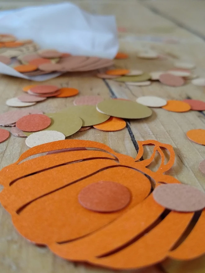Orange lasercut pumpkin confetti decoration with gold orange and brown confetti dots scattered on wooden table