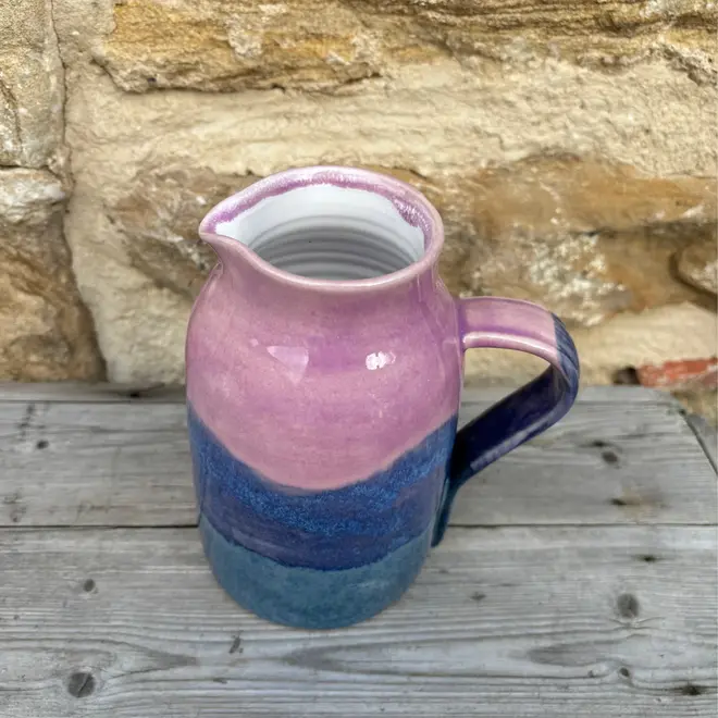 Landscape Medium Jug, a colourful jug sitting on a wooden surface against a brick backdrop. 