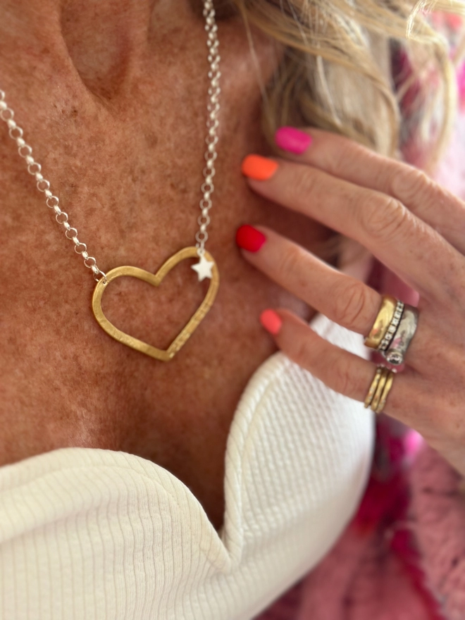 model wears large gold open heart charm on a sterling silver chain with a small silver star charm