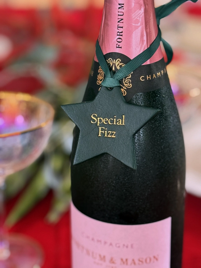 'special fizz' written in gold writing on a green leather star attached to a bottle of pink champagne.