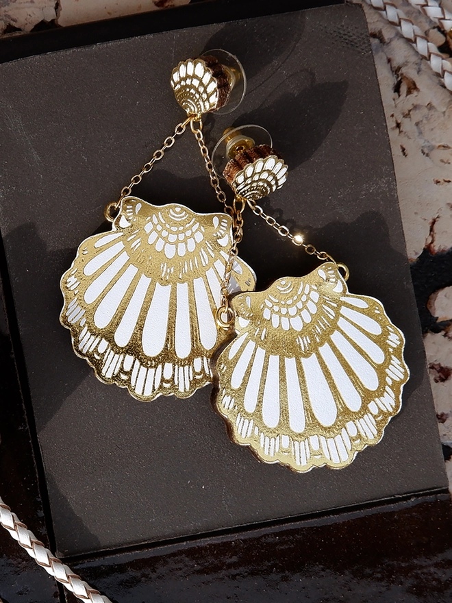 white & gold leather clamshell earrings on black tile