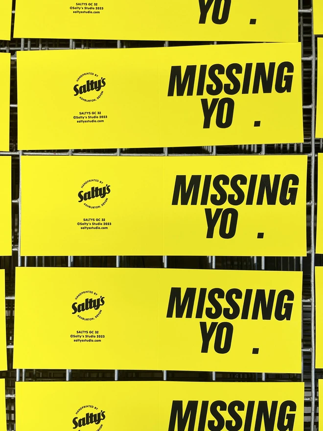 Overhead view of several bright yellow Missing You cards on a screen printing drying rack