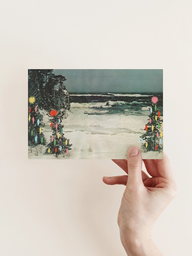 A vintage beach scene covered in snow with surrounding trees decorated with colourful fairy lights.