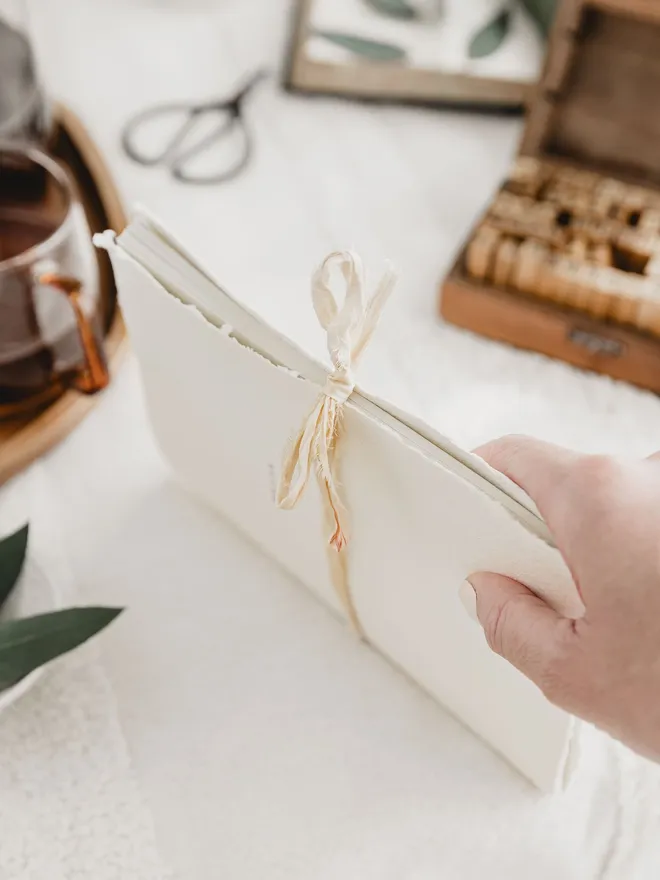 an off white journal with a deckled edge and rustic ribbon closure 
