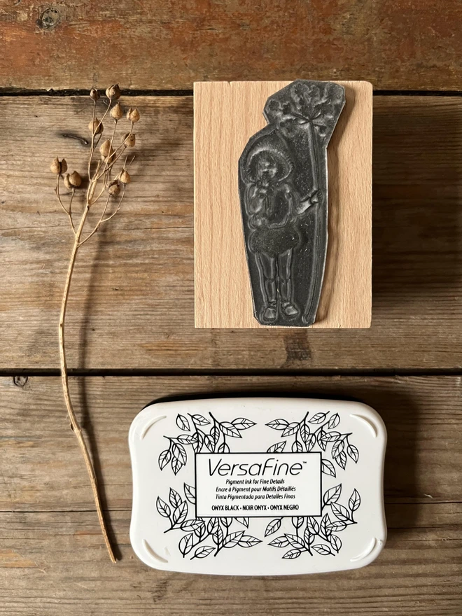 a traditional wooden rubber stamp feturing an illustration of a pixie wearing a bonnet holding a twig