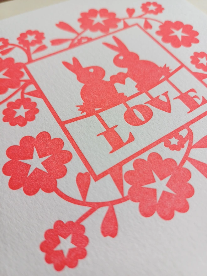 Closeup view of letterpress printed card. The red design is pressed into the paper leaving the white card raised.