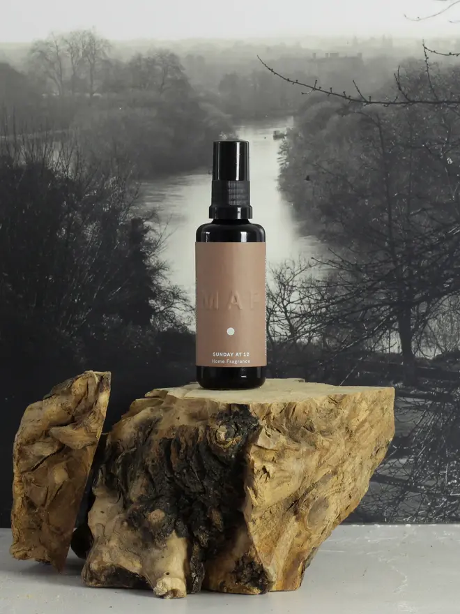 sunday at 12 sandalwood and rose home fragrance spray. bottle placed on top of rock against countryside landscape image.