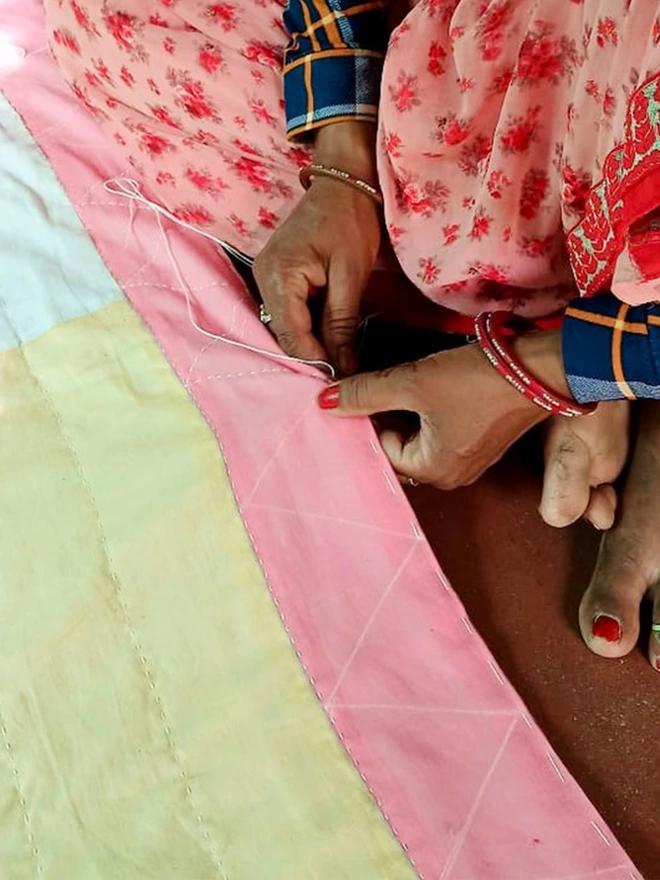 Detail of artisan's hand stitching the border on a quilt by hand