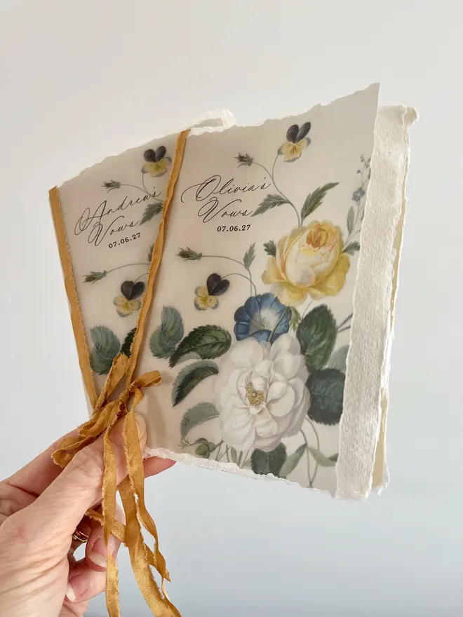 2 Floral vow booklets with the couples name, wedding date and floral design printed on vellum and tied with ribbon. The blank pages in side are handmade paper