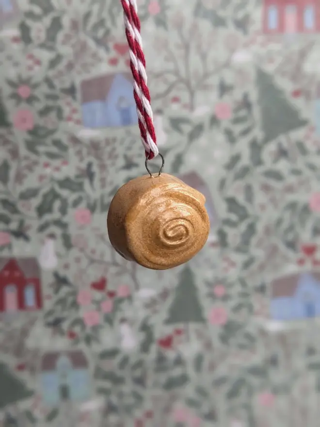 ceramic cinnamon bun christmas decoration. a close up image of a ceramic cinnamon bun hanging from red and white thread.