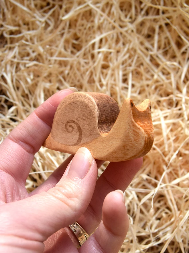 wooden toy snail being held in hand above woodwool