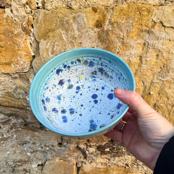 Shoreline Ramen Bowl, a person holding a colourful ramen bowl against a brick backdrop. 