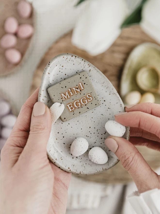 white egg shaped plate with ceramic mini eggs tag laid on top