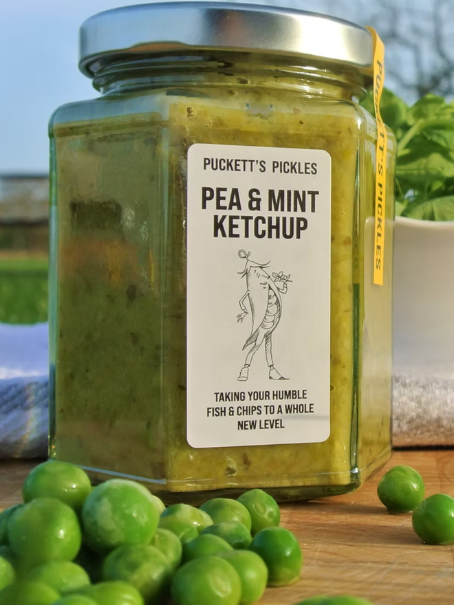 pea and mint ketchup. a jar of pea and mint ketchup photographed with peas in the foreground.