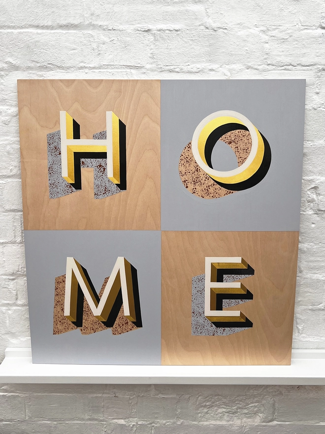 HOME hand painted sign in 23 carat gold leaf, pale blue, off white, tan, against a white brick wall, straight on. 