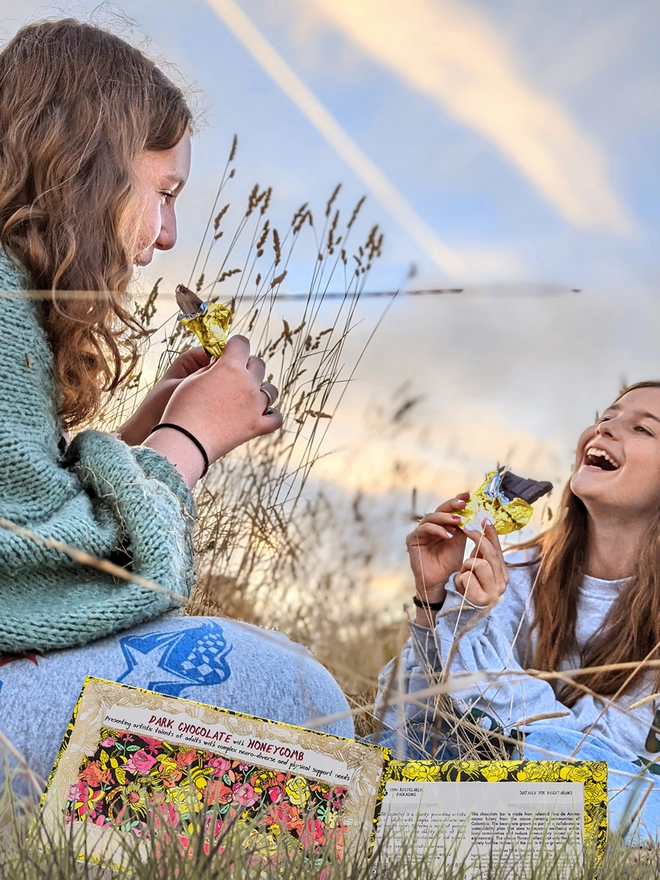 Two happy girls in a field enjoying charity dark chocolate bar wrapped in gold foil