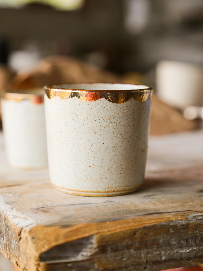 white stoneware drinking beaker with gold scallop decoration around the rim
