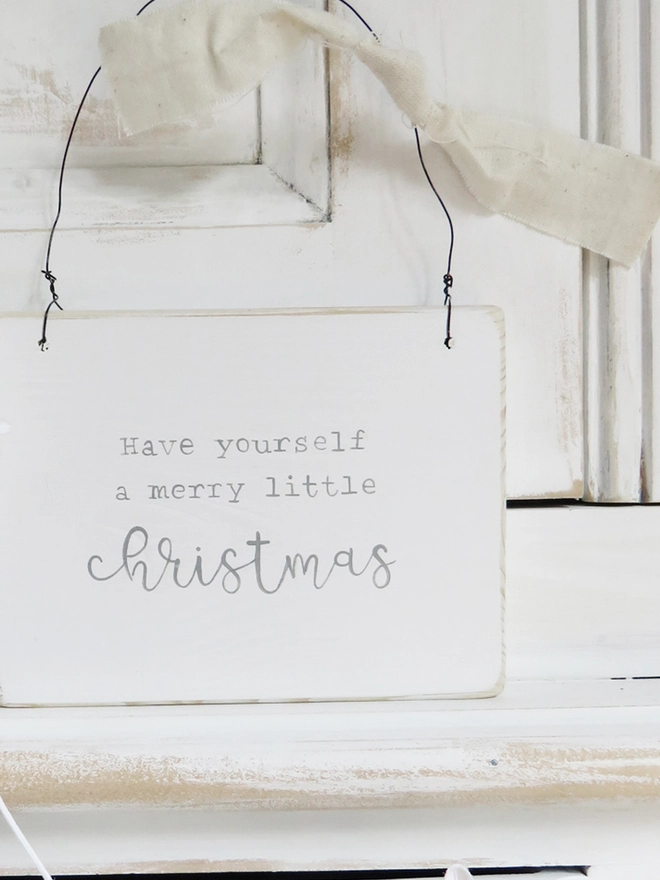 white wooden sign painted with a merry little Christmas massage hung on wire and decorated with ribbon