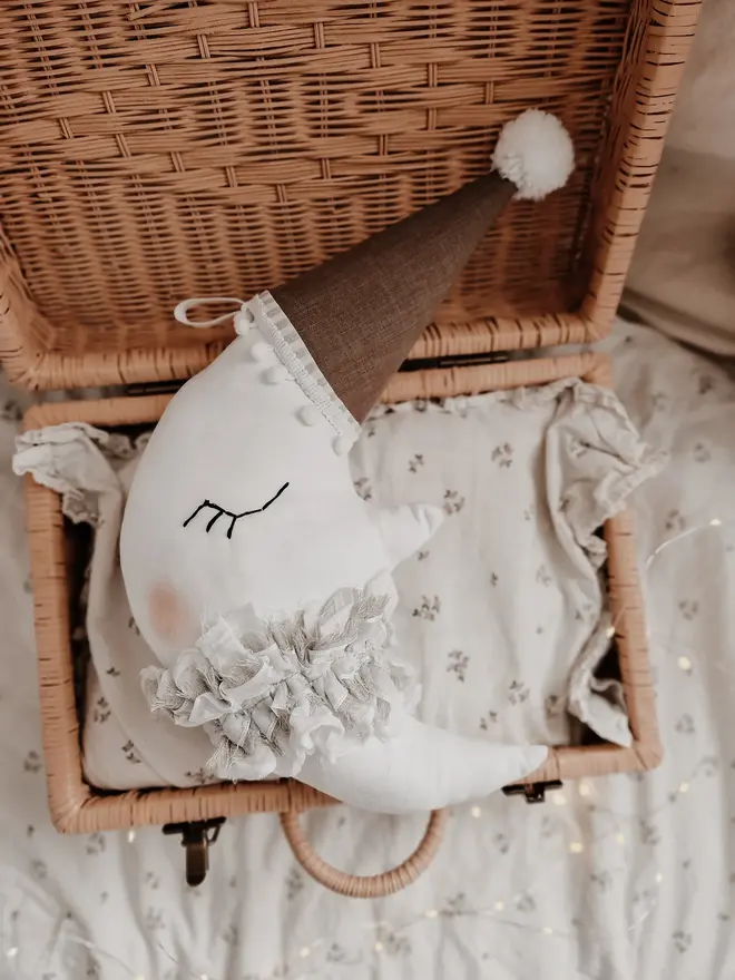 Hanging Moon Pillow Decoration, a hanging moon pillow decoration sitting in a wooden hamper amongst other bed accessories. 