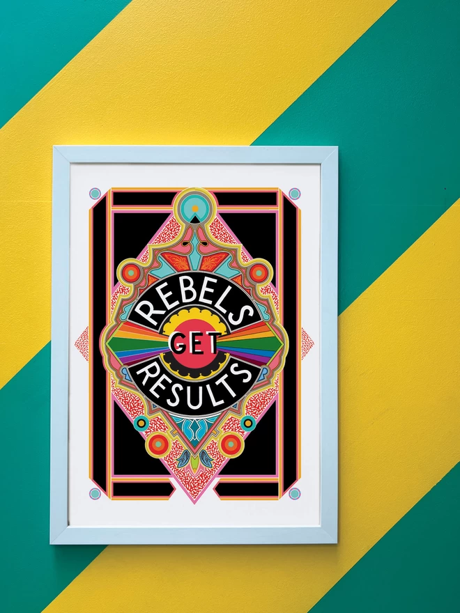 Rebels Get Results is written in white on a black background at the centre of this vibrant, abstract portrait illustration, with a black background and rainbows emitting from the centre, and multi-coloured detailing. The picture is hanging in a white portrait frame against a wall painted with thick diagonal green and yellow stripes.