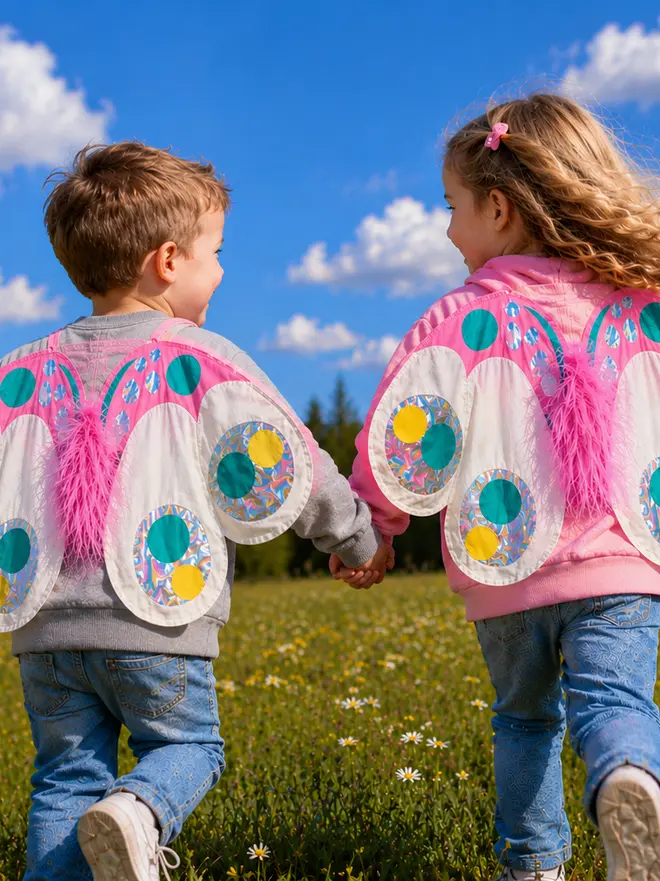 A small boy and his sister are running through a field on a sunny day, wearing sweatshirts with a butterfly on the back