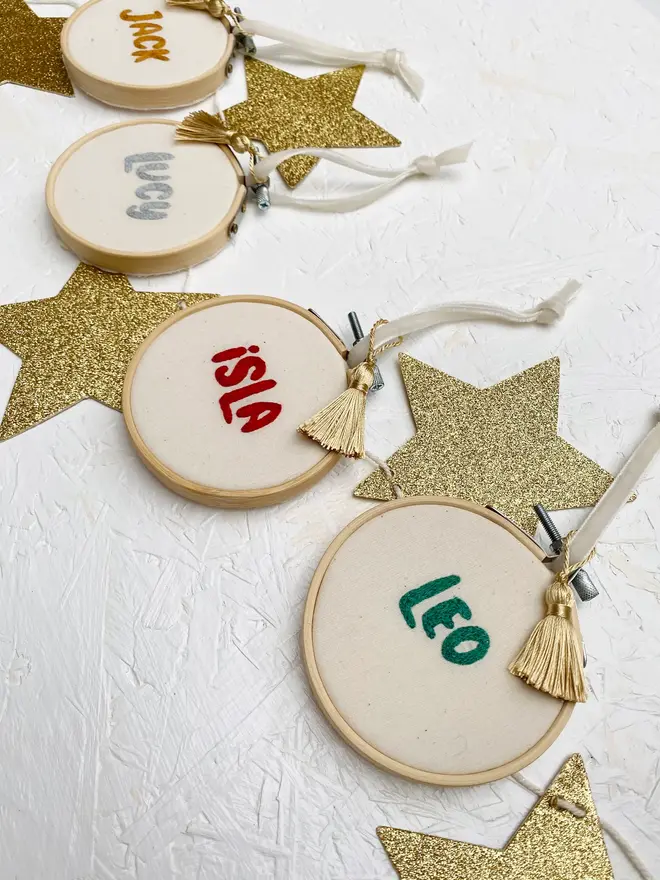 personalised name embroidered hoop bauble. set of 4 embroidered hoop baubles strung up on white wall.