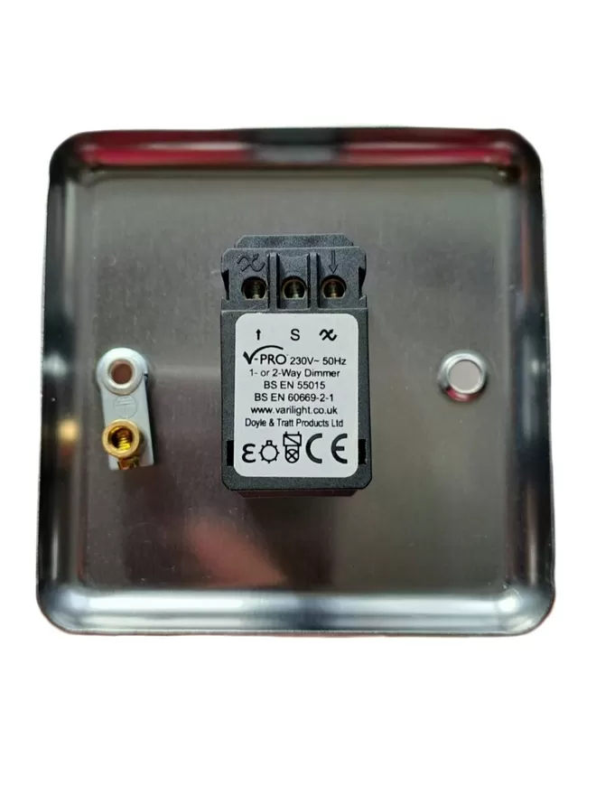 The back of a brushed chrome light switch plate, there is a black rectangle LED dimmer switch module in the centre of the switch plate, the module has three round holes at it’s base for wires and a white label with V Pro, 230v – 50Hz 1 or 2 way Dimmer, BS EN 55015, BS EN 60669 – 2- 1 www.varilight.co.uk, Doyle & Tratt products Ltd written on it, there are two screw holes in the light switch, the hole on the left also has an earthing screw on it. The children’s light switch brand is Candy Queen Designs.